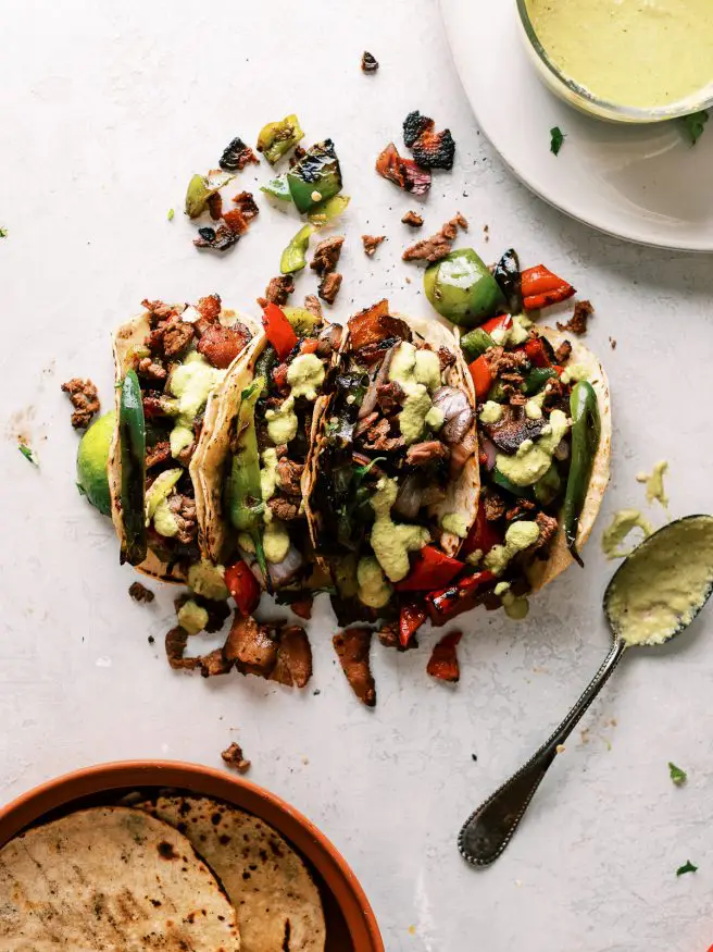 Alambre tacos are Carne Asada topped with bacon, and grilled onions and peppers, topped with a roasted pepper and green sauce and stuffed into a taco. Do I have your attention yet?