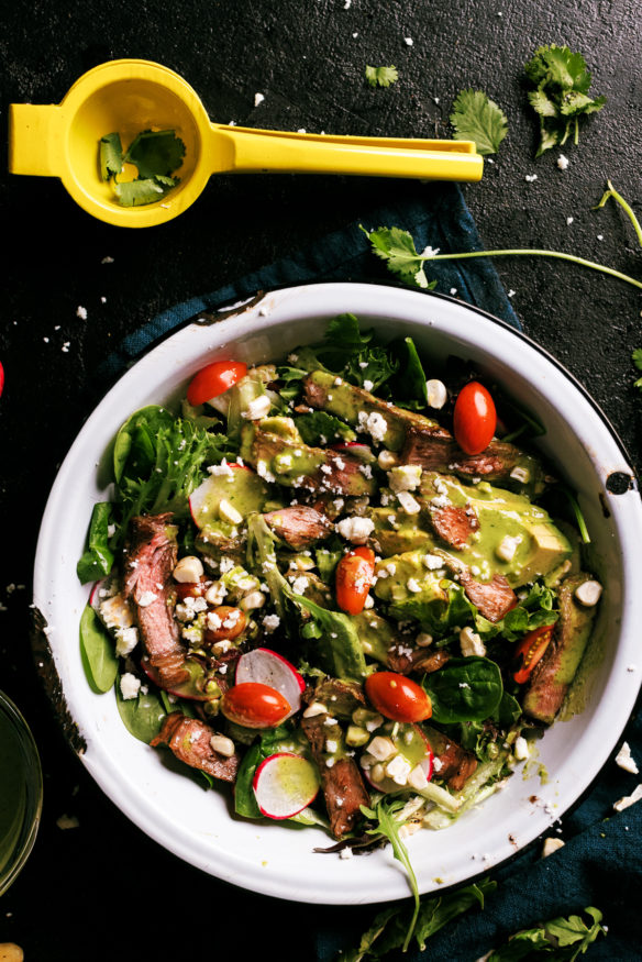 A seared steak salad topped with a fresh cilantro lime vinaigrette topped with fire roasted corn, ripe cherry tomatoes and radishes.