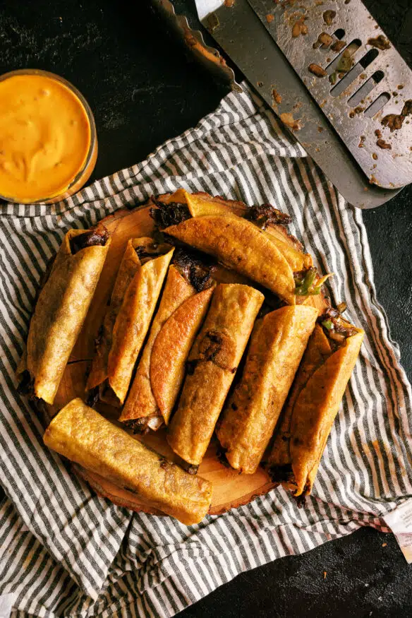 Philly cheesesteak taquitos recipe with thinly sliced ribeye steak, cheese, onions and bell pepper grilled on the Blackstone griddle. 