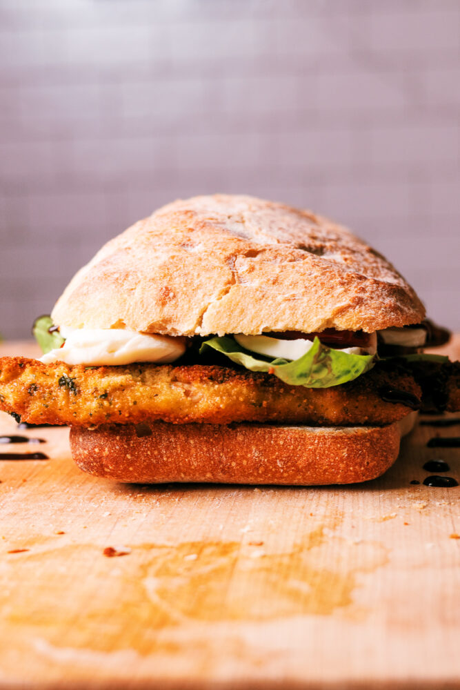 Crispy chicken Caprese sandwich with pesto, roasted tomatoes, fresh mozzarella, and balsamic glaze on toasted ciabatta bread.